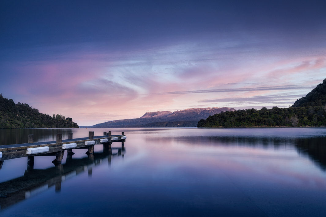 Evening dusk light at sunset over the lake with a jetty in the foreground and mountains beyond