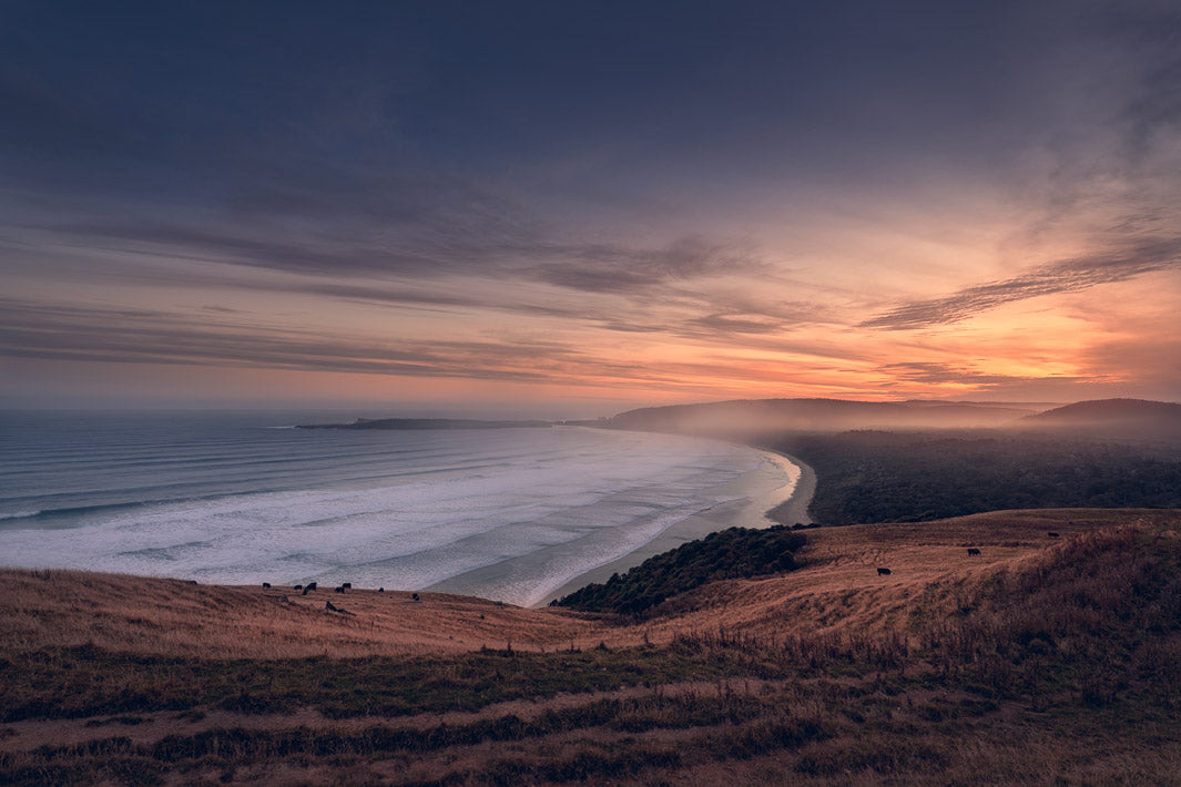 Lookout at dusk over misty hills and grass to the beach below