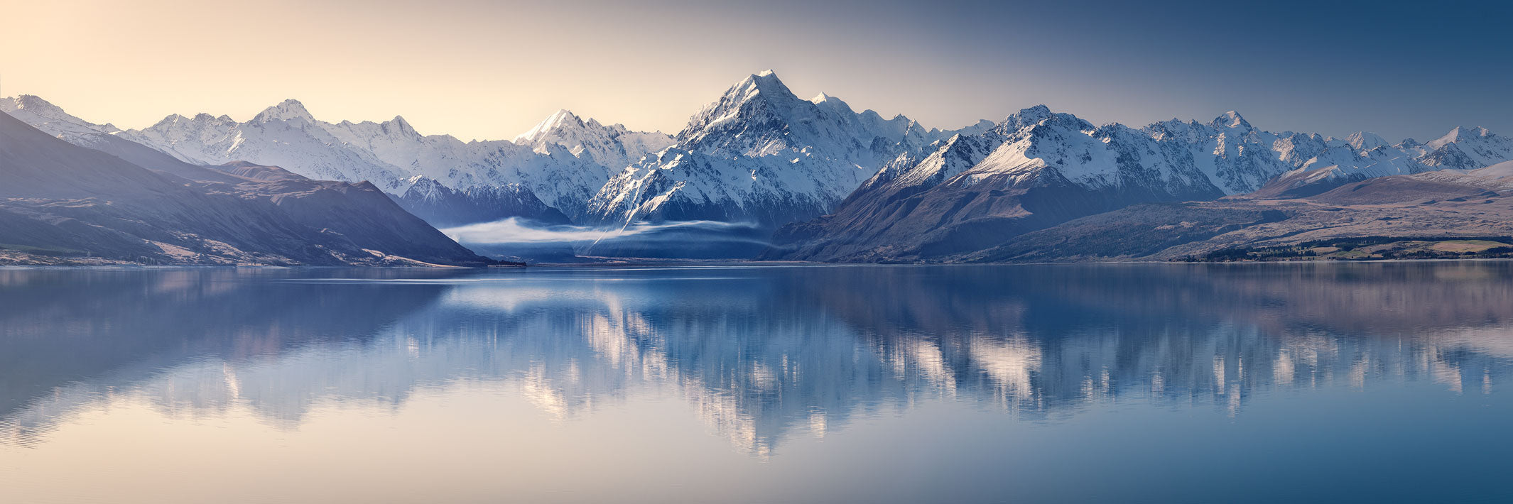 Panoramic landscape photo of snow covered mountains and Aoraki Mt Cook, reflected in the still water of Lake Pukaki.