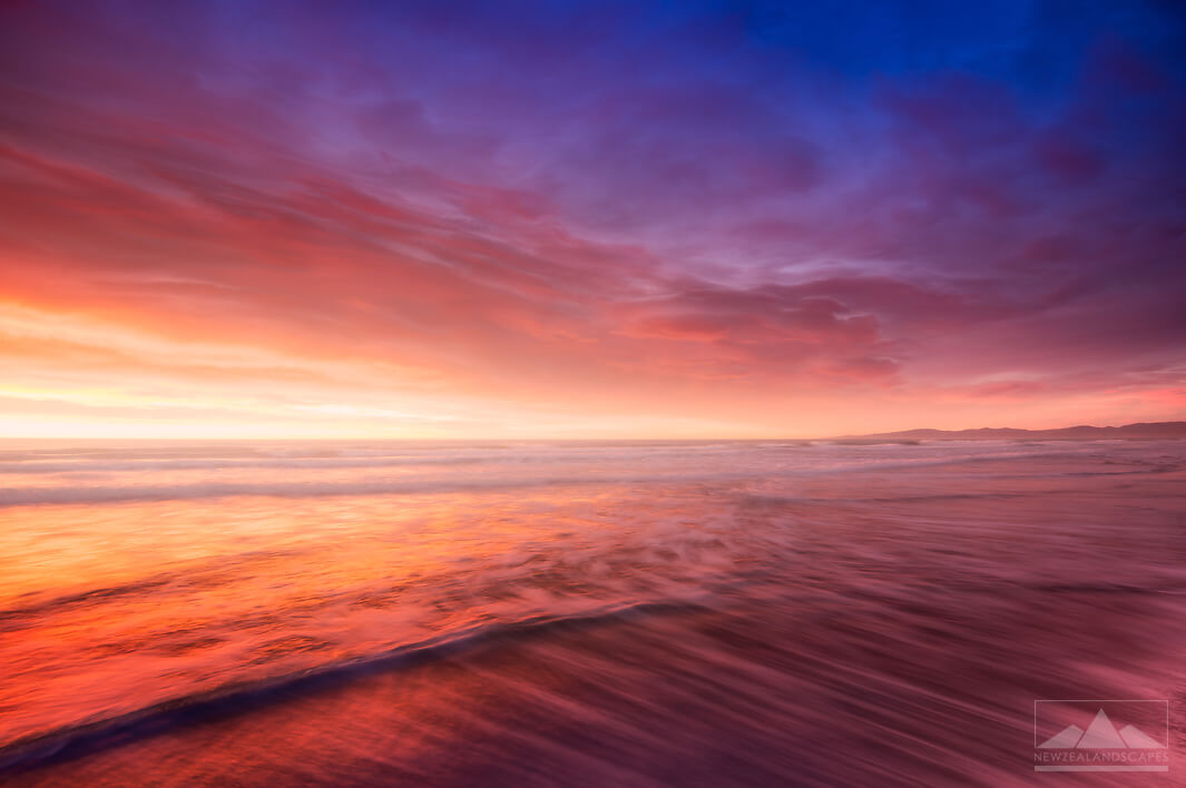 Vibrant sunrise colours of pinks, reds and blues in the sky and clouds reflected in the sea below