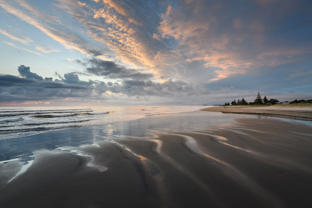 Pink coloured clouds with the beach below and ripples of streams running through the sand.